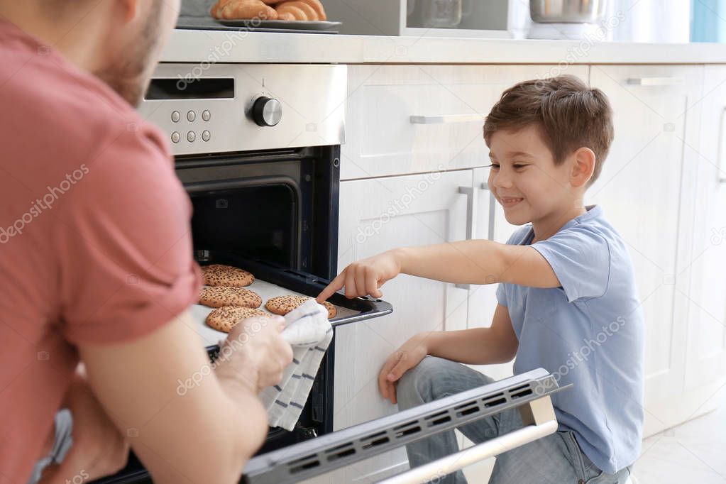 Little boy watching his father bake cookies in oven indoors