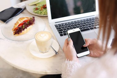 Kafede masada cep telefonu kullanan genç kadın