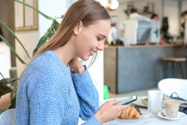 Kafede masada cep telefonu kullanan genç kadın