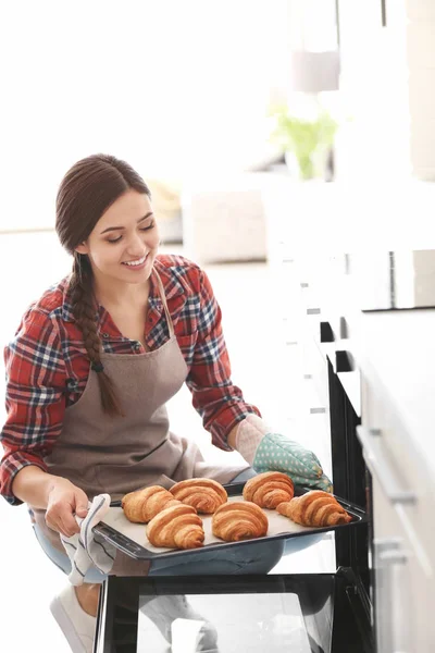 Женщина берет свежеиспеченные круассаны из духовки в помещении — стоковое фото