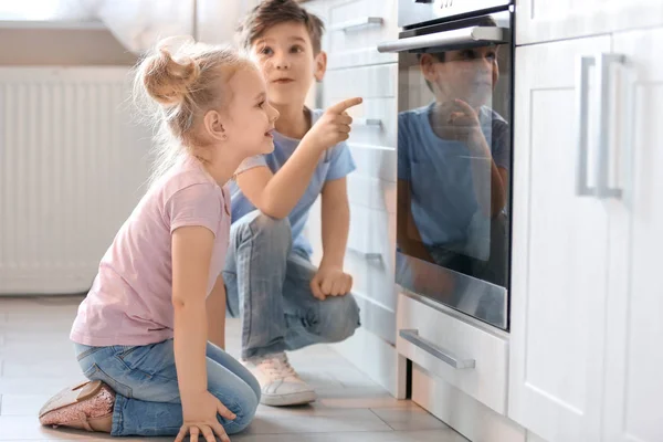 Little kids sitting near oven indoors
