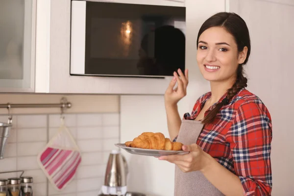Mulher colocando prato com croissants no microondas dentro de casa — Fotografia de Stock