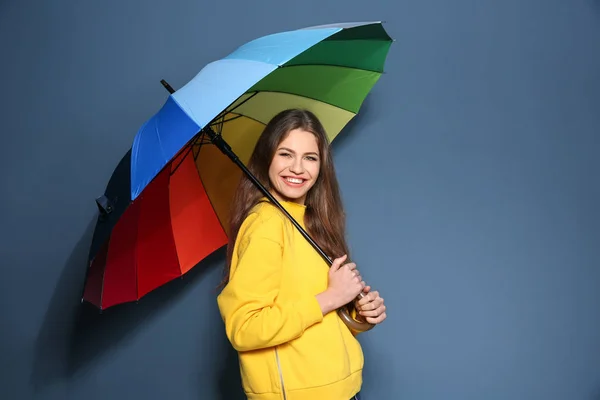 Giovane donna con ombrello arcobaleno su sfondo colore — Foto Stock