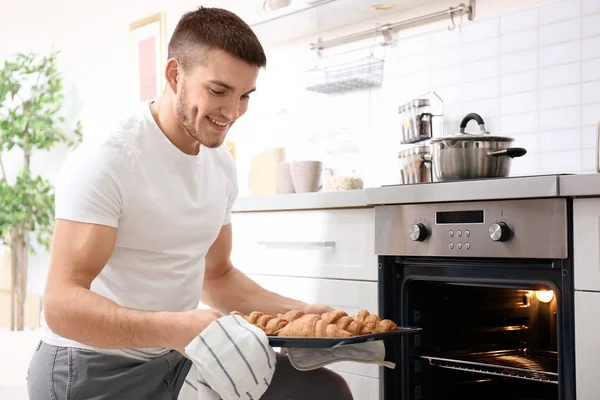 Young man baking croissants in oven indoors