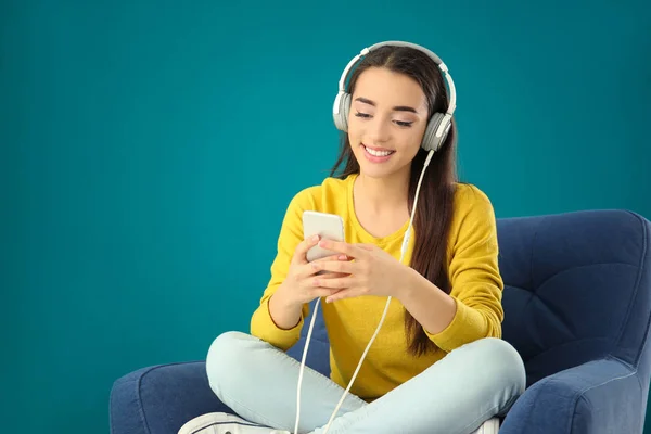 Schöne junge Frau hört Musik, während sie im bequemen Sessel vor farbigem Hintergrund sitzt — Stockfoto