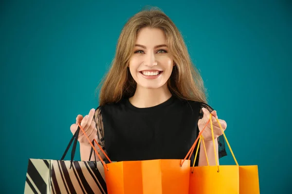 Schöne junge Frau mit Einkaufstaschen auf farbigem Hintergrund — Stockfoto