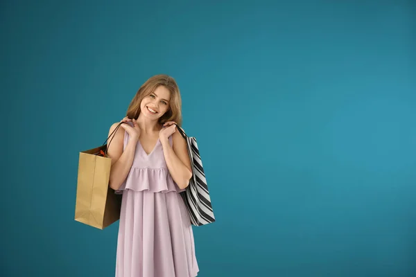 Hermosa mujer joven con bolsas de compras en el fondo de color — Foto de Stock