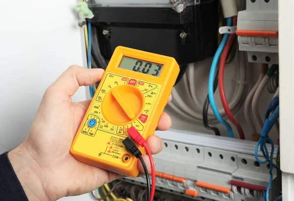 Молодой электрик измеряет напряжение в распределительной плате, крупный план — стоковое фото