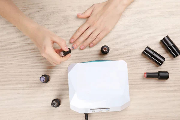 Mujer haciendo manicura cerca de la lámpara ultravioleta en la mesa — Foto de Stock