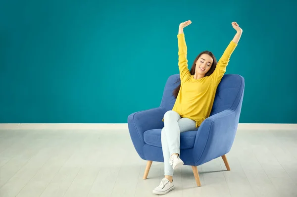 Hermosa joven mujer relajante en cómodo sillón contra la pared de color — Foto de Stock