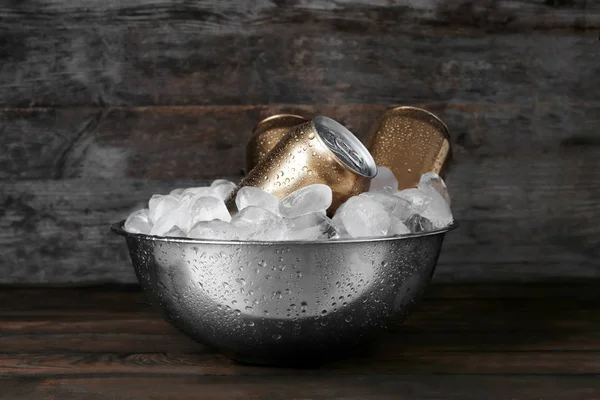 Bowl with cans of beer and ice on wooden background