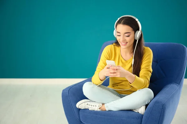 Красивая молодая женщина слушает музыку, сидя в удобном кресле у цветной стены — стоковое фото