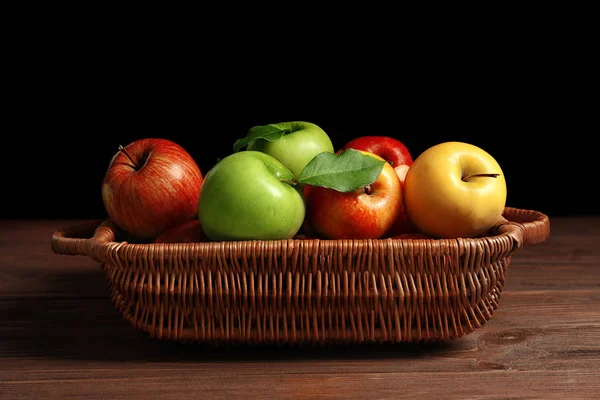 Saftige Äpfel im Korb auf dem Tisch vor dunklem Hintergrund — Stockfoto