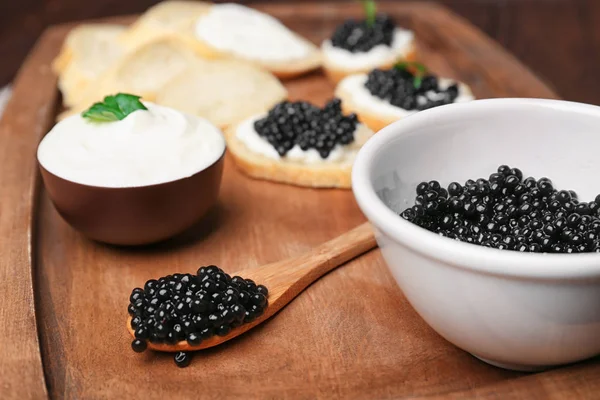 Cuenco y cuchara con delicioso caviar negro sobre tabla de madera —  Fotos de Stock