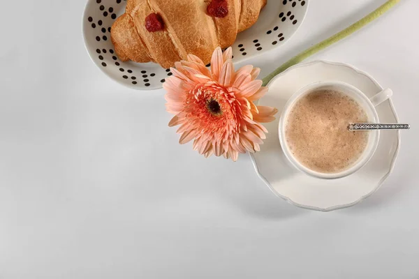 Plate with croissant, cup of coffee and flower on table, top view. Tasty breakfast