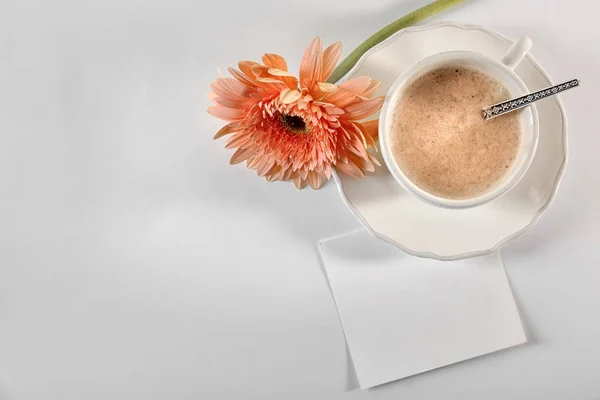 Cup of coffee for breakfast, flower and empty card on table, top view