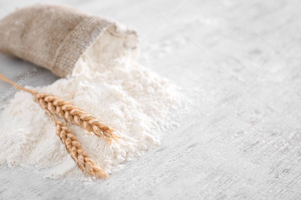 Bag with flour on wooden table, food background