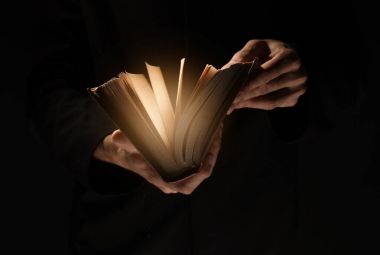 Priest with old Bible on black background, closeup clipart