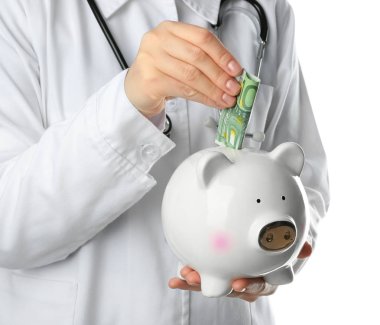 Genç kadın doktor seramik kumbara beyaz arka plan içine para koyarak