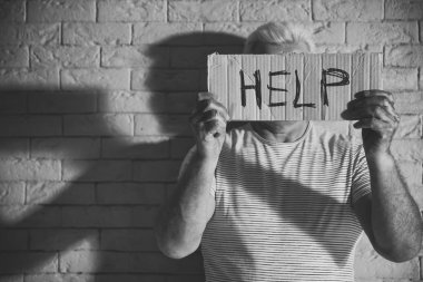 Poor man holding sign with word HELP on brick wall background. Black and white effect clipart