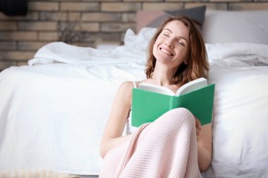 Evde yatak yakınındaki kitap ile güzel gülümseyen kadın