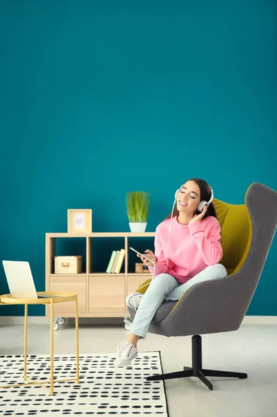 Красива молода жінка слухає музику, сидячи в зручному кріслі вдома — стокове фото