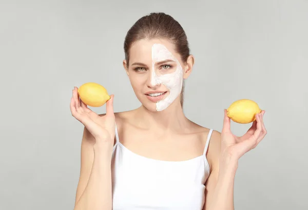 Belle jeune femme avec masque facial et citrons mûrs sur fond gris — Photo