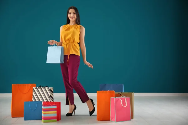 Mujer joven feliz con bolsas de compras contra la pared de color —  Fotos de Stock