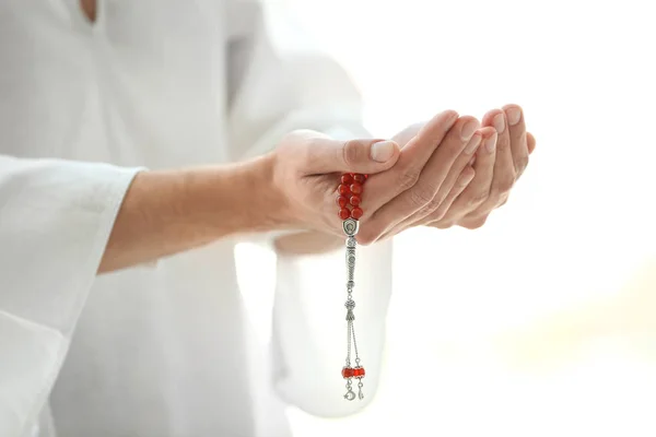 Young Muslim man with beads praying on light background