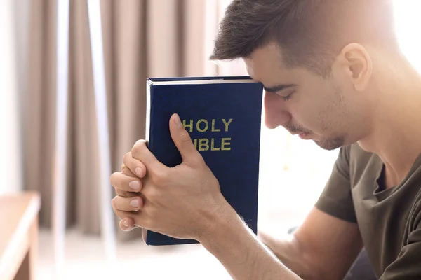 Jovem religioso com a Bíblia orando em casa — Fotografia de Stock