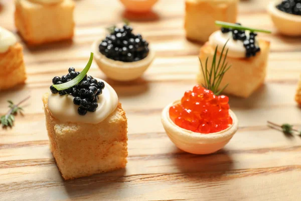 Canapés deliciosos com caviar preto e vermelho na mesa de madeira — Fotografia de Stock