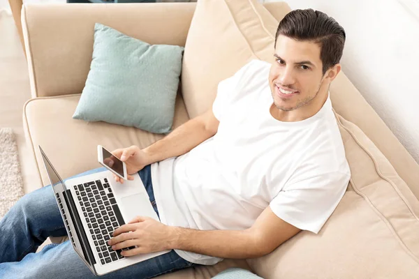 Junger Mann benutzt Smartphone bei der Arbeit mit Laptop im Home Office — Stockfoto