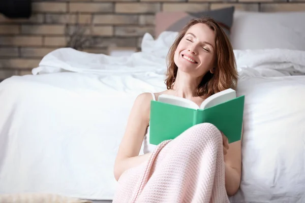 Mulher sorridente bonita com livro perto da cama em casa — Fotografia de Stock