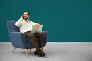Renk duvara rahat koltuk içinde otururken cep telefonu üzerinde konuşurken laptop ile yakışıklı adam