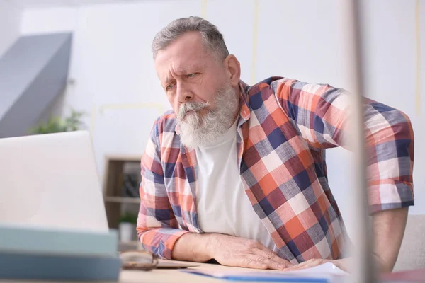 Старший человек работает с ноутбуком за столом в офисе — стоковое фото