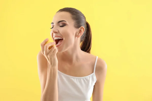 Beautiful young woman eating ripe lemon on color background — Stock Photo, Image