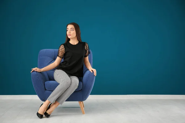 Piękna młoda kobieta, siedząc w wygodnym fotelu kolorów muru — Zdjęcie stockowe