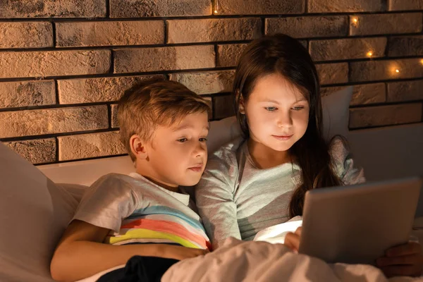 Ładny mały brat i siostra, czytania na dobranoc z komputera typu tablet w godzinach wieczornych — Zdjęcie stockowe