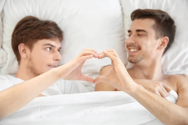 Fiatal meleg pár, így szív szimbólum a kezüket, miközben az ágyban fekve — Stock Fotó