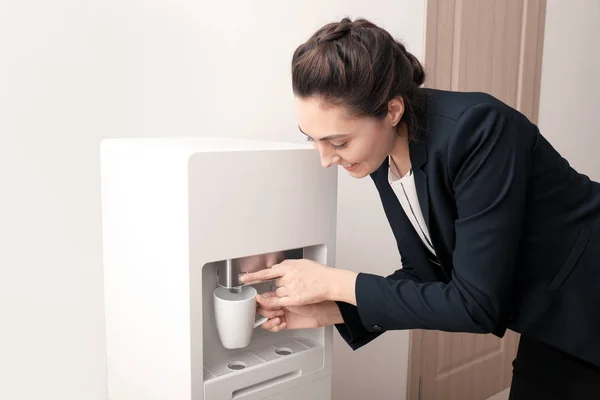 Woman filling cup from water cooler in office — Stock Photo, Image