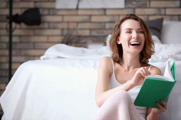 Mulher sorridente bonita com livro perto da cama em casa — Fotografia de Stock