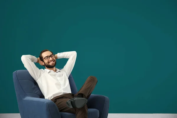 Homem bonito relaxando em poltrona confortável contra parede de cor — Fotografia de Stock