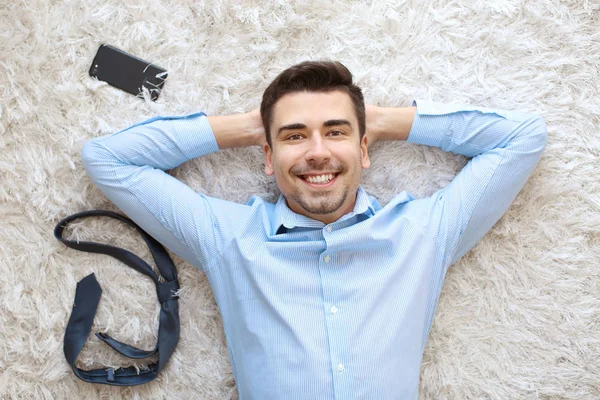 Joven con teléfono y corbata acostado en la alfombra, vista superior —  Fotos de Stock