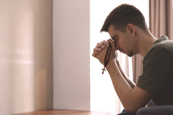 Jovem religioso com rosário rezando em casa — Fotografia de Stock
