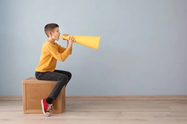 Divertido niño sentado en cubo de madera y gritando en el megáfono de papel en el interior —  Fotos de Stock