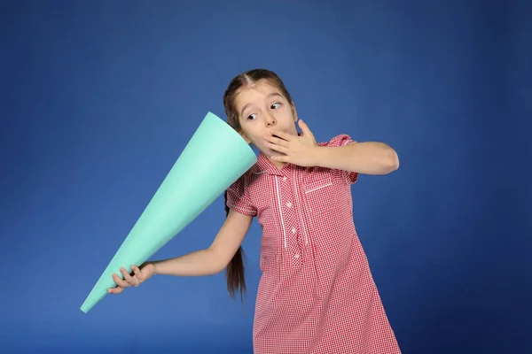 Эмоциональная маленькая девочка с бумажным мегафоном на цветном фоне — стоковое фото