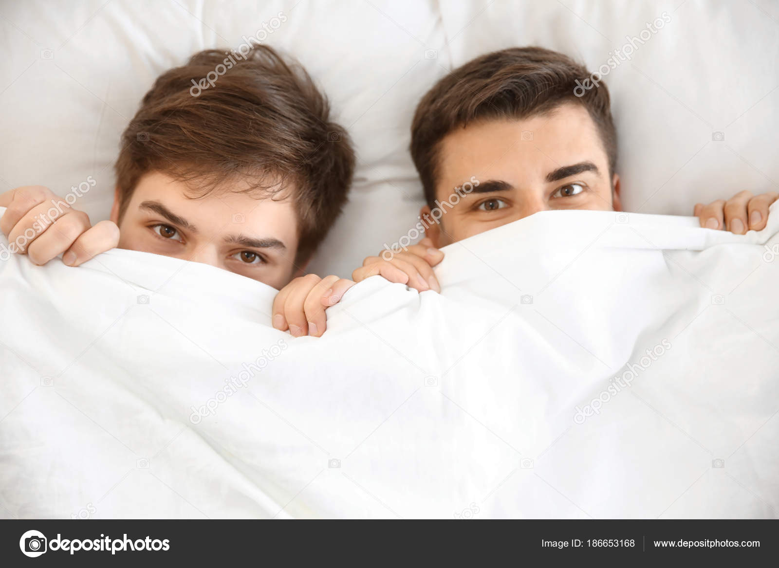 Young gay couple hiding under blanket in bed together — Stock Photo