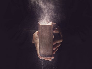 Priest with old Bible on black background, closeup clipart