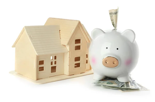 Piggy banco de cerâmica com dinheiro e modelo de casa no fundo branco — Fotografia de Stock