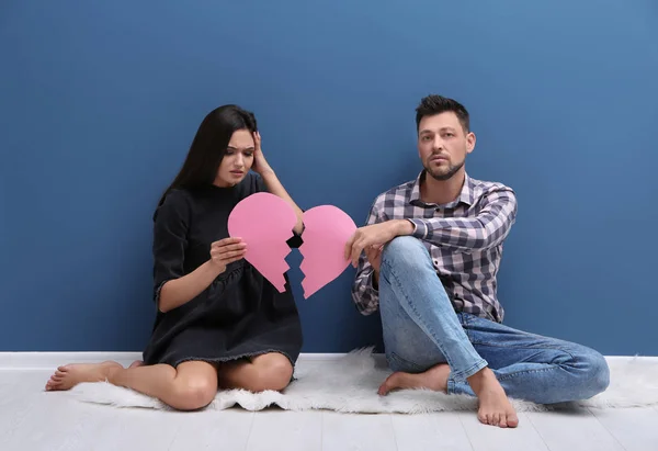 Jovem casal segurando papel coração cortado ao meio perto da parede de cor. Problemas de relacionamento — Fotografia de Stock